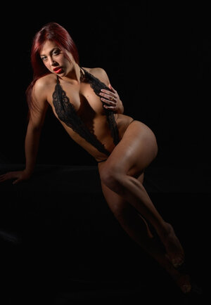 Passionate red-haired porn model posing in sexy black peignoir in the black room